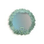 Round hanging mirror with a decorative leaf and floral frame in soft green tones.