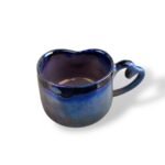 Heart-shaped ceramic mug with a glossy, deep blue glaze that shifts into a lighter blue, featuring a uniquely curled handle.