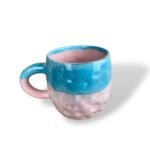 Ceramic mug with a dimpled texture, glazed with bright turquoise on the top half and handle, and soft pink on the bottom half and inside.