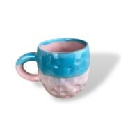 Ceramic mug with a dimpled texture, glazed with bright turquoise on the top half and handle, and soft pink on the bottom half and inside.