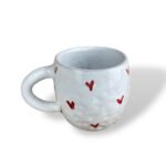 White textured ceramic mug decorated with small, hand-painted red heart shapes scattered across the surface.