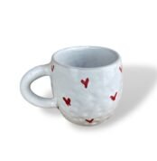 White textured ceramic mug decorated with small, hand-painted red heart shapes scattered across the surface.
