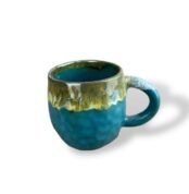 Textured teal ceramic mug with a flowing golden and earthy glaze around the rim and handle, resembling molten metal over rugged terrain.