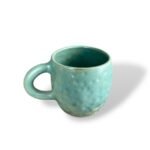 Matte turquoise ceramic mug with a gently dimpled texture and a softly rounded handle, evoking an aged, handcrafted aesthetic.