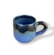 Glossy ceramic mug with a deep blue base and shimmering dark glaze, resembling a night sky over water.