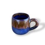 Handcrafted ceramic mug with matte blue base and flowing sand-brown glaze, inspired by river landscapes.