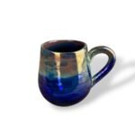 Glossy ceramic mug with a reflective gold and deep blue glaze, highlighting elegant curves and radiant finish.