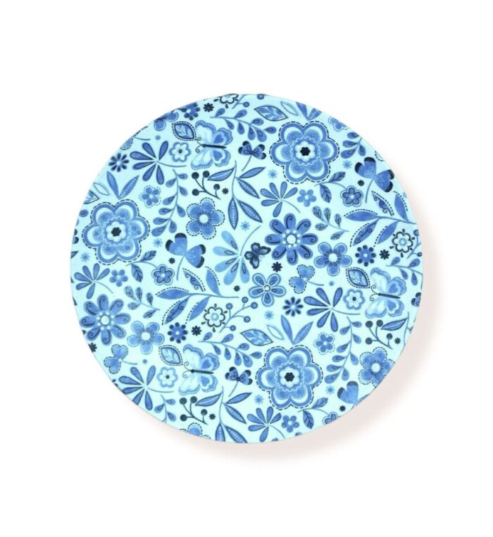 Round blue floral coaster with detailed blue flower and leaf patterns, flat view under bright lighting.