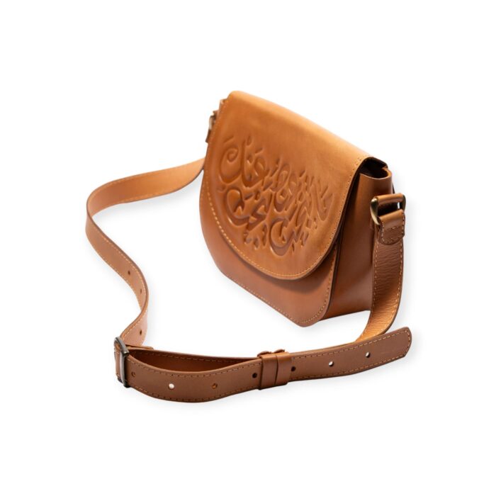 Angled view of brown small crossbody leather bag with Arabic calligraphy engraving and adjustable strap.