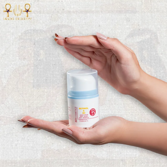 Retinol and Vitamin B3 night serum in a white 30ml pump bottle with blue accents, held between two hands on a textured background.