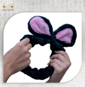 Two hands stretching the black Bunny Clasp with pink inner ears against a white background