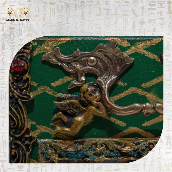 Detailed view of a small gold cherub ornament on the green patterned surface of the Cabinet of Secrets.
