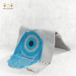 Side view of the Eye of Light bag with handcrafted blue eye bead embroidery and flowing turquoise fringes on a light fabric base.