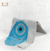 Side view of the Eye of Light bag with handcrafted blue eye bead embroidery and flowing turquoise fringes on a light fabric base.