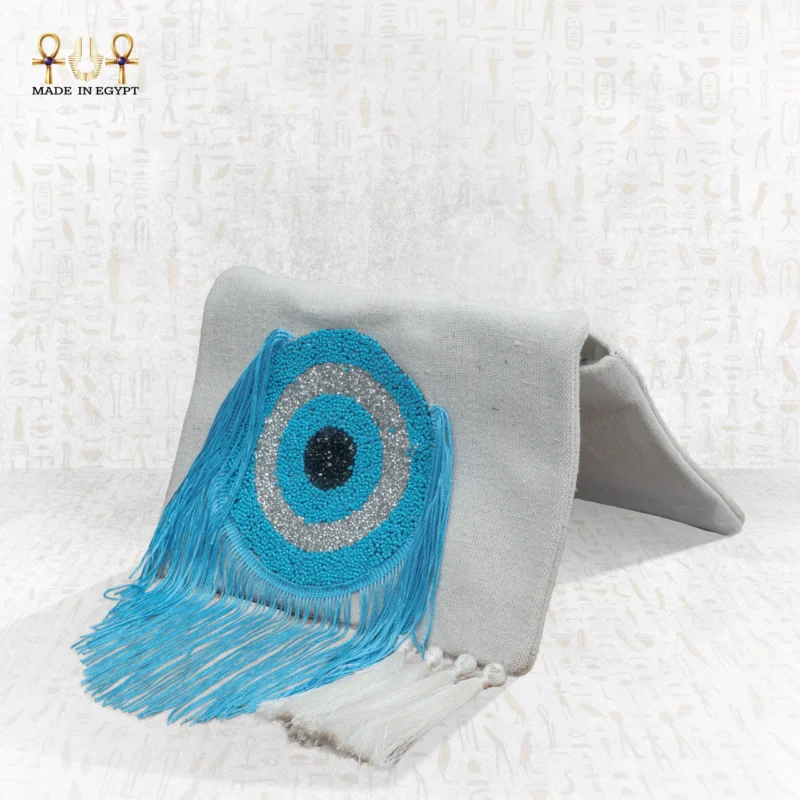 Side view of the Eye of Light bag with handcrafted blue eye bead embroidery and flowing turquoise fringes on a light fabric base.