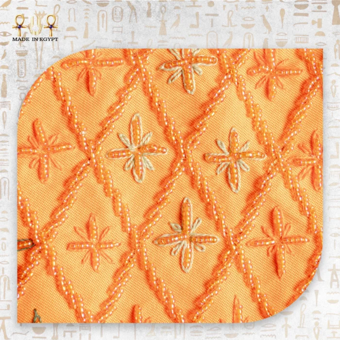 Close-up of orange embroidered fabric with beadwork creating diamond and floral patterns.