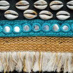 Close-up of Nubian Pearl bag showing natural shells, turquoise embroidery, golden woven trim, and white fringes.