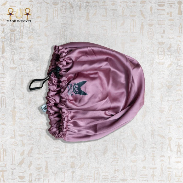 Pink satin sleeping bonnet with adjustable strap on display.
