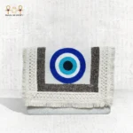 Front view of the Guardian Eye clutch featuring bold blue evil eye embroidery with textured silver and cream fringes.