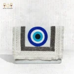Front view of the Guardian Eye clutch featuring bold blue evil eye embroidery with textured silver and cream fringes.