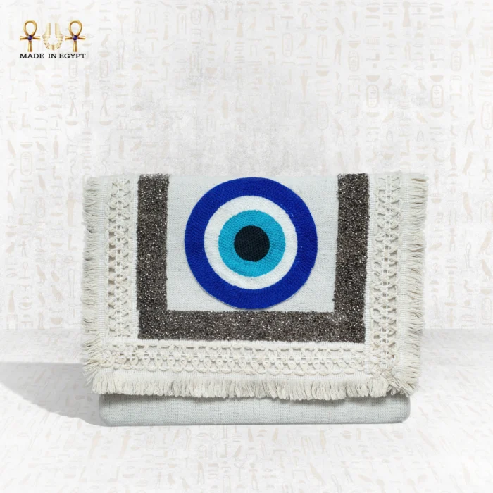 Front view of the Guardian Eye clutch featuring bold blue evil eye embroidery with textured silver and cream fringes.