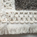 Close-up of the Guardian Eye bag showing cream handwoven fringe with intricate silver-thread embroidery.