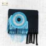 Front view of the Turquoise Eye clutch bag, showing circular turquoise, silver, and black bead embroidery with flowing blue and black fringes.