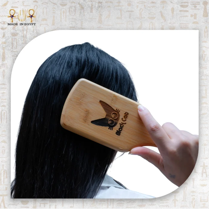 Wooden paddle brush being used to comb long black hair.