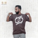 Man wearing a brown oversized Fusion Tee T-Shirt by Hook with white graphic print and Egyptian motif background