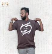 Man wearing a brown oversized Fusion Tee T-Shirt by Hook with white graphic print and Egyptian motif background