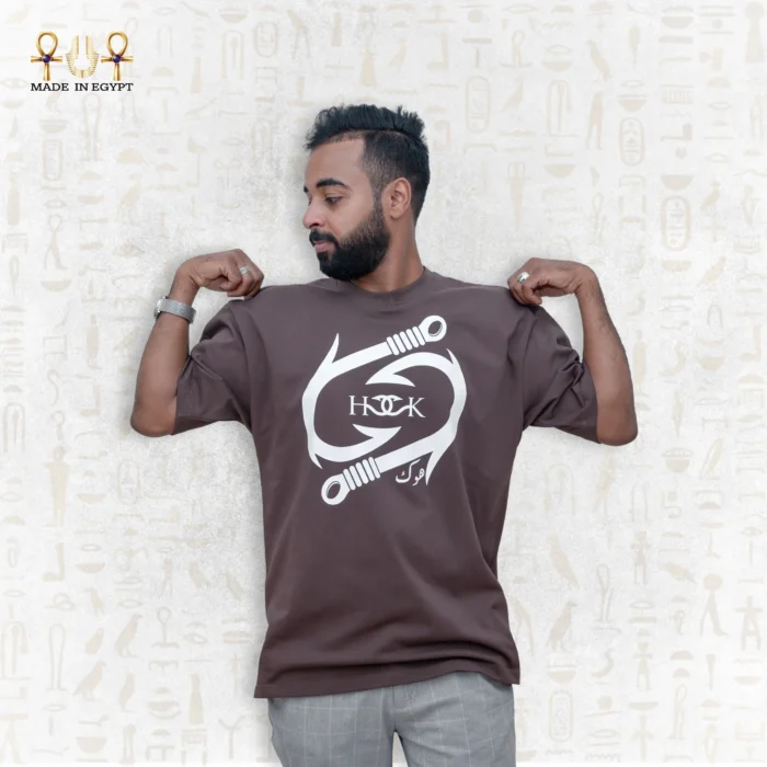Man wearing a brown oversized Fusion Tee T-Shirt by Hook with white graphic print and Egyptian motif background