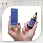 Hands holding Queen rosemary essential oil bottle and packaging box against a light fabric background.