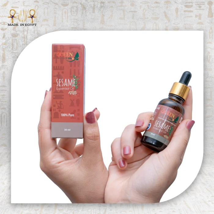 Hands holding Queen sesame essential oil bottle and packaging box against a light fabric background.