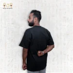 Wider side back view of a man wearing a black Skyline Tee, hands behind his back, showing more of the shirt’s length.