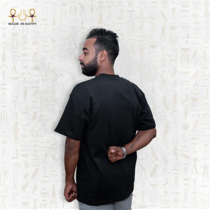 Wider side back view of a man wearing a black Skyline Tee, hands behind his back, showing more of the shirt’s length.